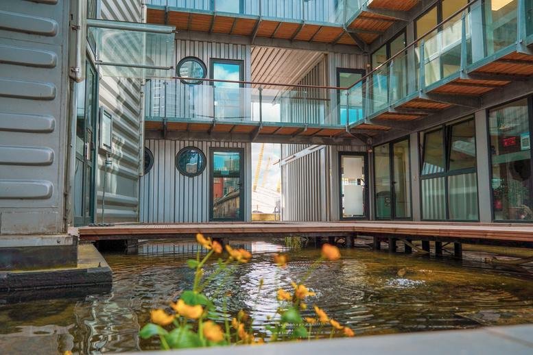 Exterior courtyard of 64, Orchard Place, Trinity Buoy Wharf featuring shipping container offices and a pond.