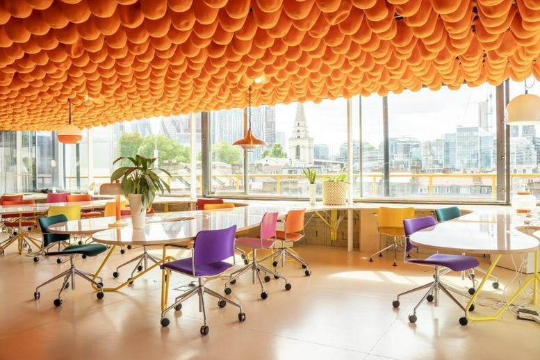 Spacious sunlit communal workspace with a textured orange ceiling and colorful chairs at 68-80, Hanbury Street.