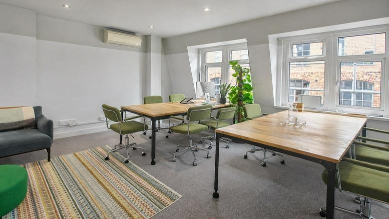 Meeting room at 75, Dean Street featuring light wood tables, green chairs, and a colourful striped rug.