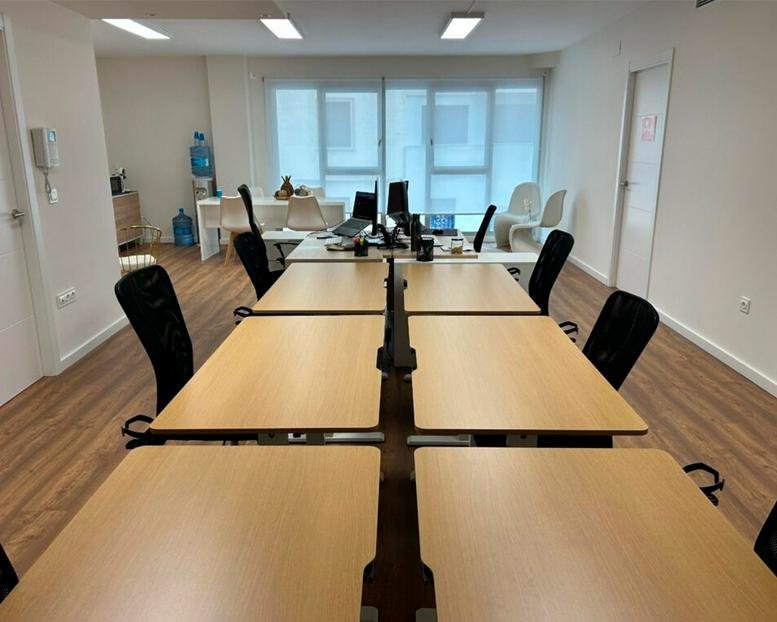 Spacious open-plan workspace at 77, Carrer de Cerdà de Tallada with light wood desks and black chairs.