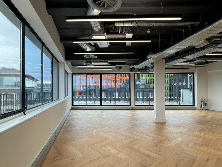 Spacious open-plan office area with herringbone wood flooring and large windows.