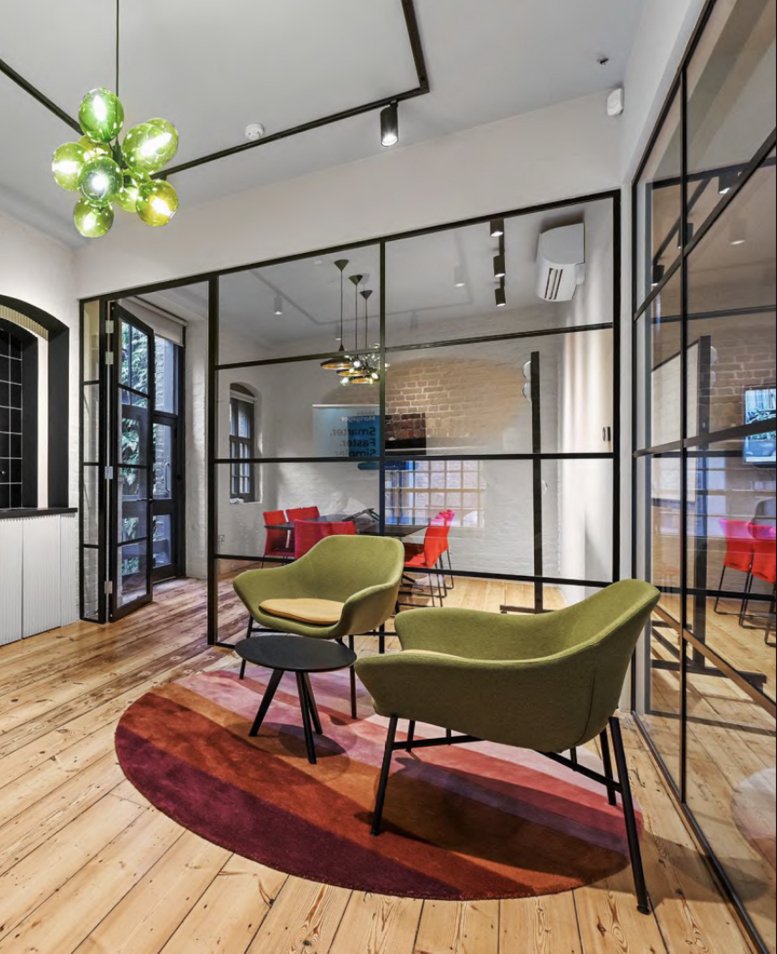 Colorful breakout lounge at 81a, Endell Street with green velvet armchairs and a vibrant circular rug.