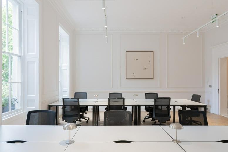 Modern open-plan office with rows of white desks and black ergonomic chairs.