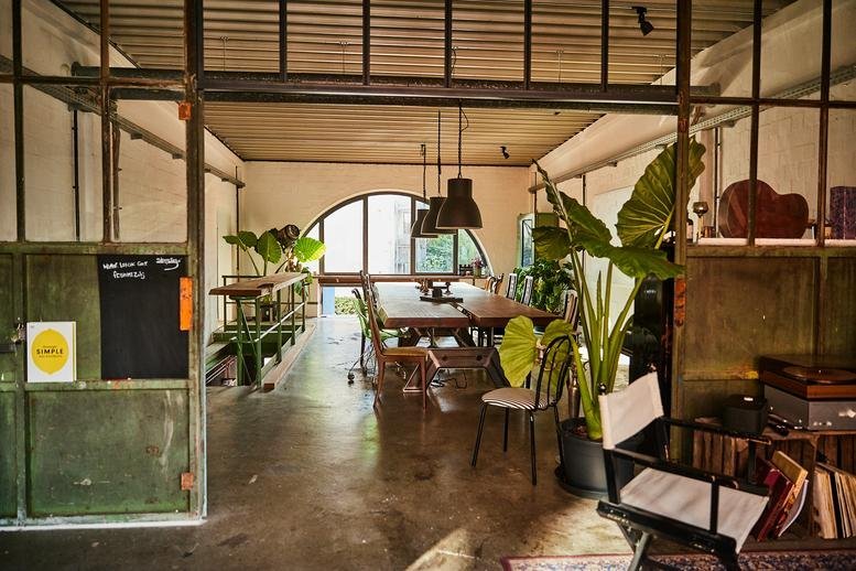 Spacious industrial communal area with wooden tables and large plants at 93, Lerchenstraße.