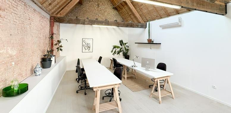 Spacious open-plan workspace with white trestle desks and high timber-beam ceilings.