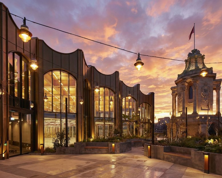 Exterior facade of Arding & Hobbs at sunset with lit windows and a historic clock tower.