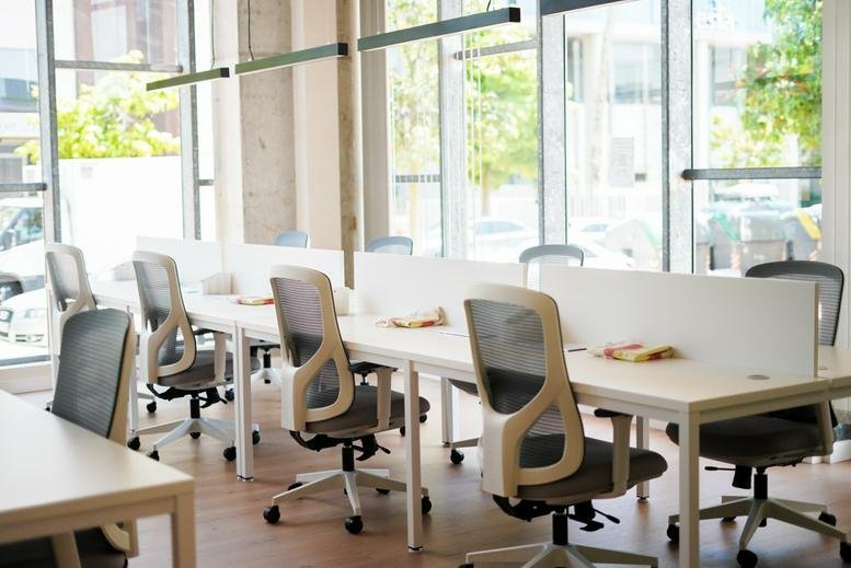 Open-plan coworking space with rows of white desks and grey ergonomic chairs.