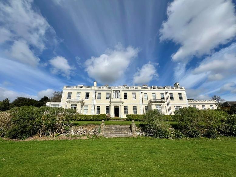 Exterior view of the white stately facade of Barham Court set against a blue sky.