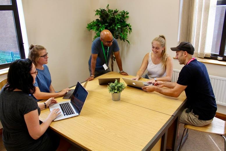 People collaborating around a wooden table in a bright office space at Basing House, 46, High Street.