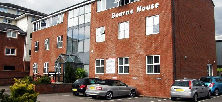 Exterior view of the red brick Bourne Business Centre with glass entrance and parked cars.