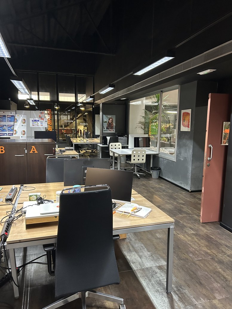 Open-plan workspace at Carrer de Pujades,146 featuring wooden desks and black ergonomic chairs.