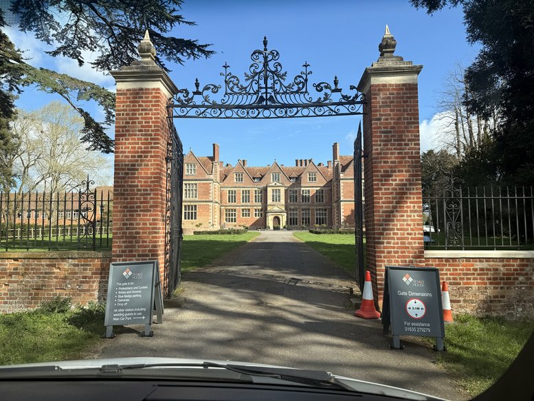Exterior view of the grand manor house at Church Road seen through a decorative iron gate