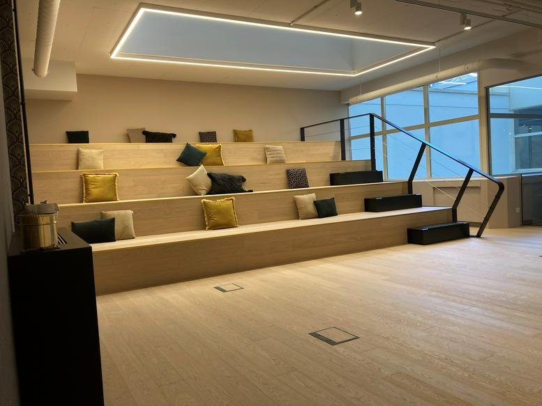 Spacious communal arena at 14-16 avenue Pasteur with wooden tiered seating and yellow pillows.