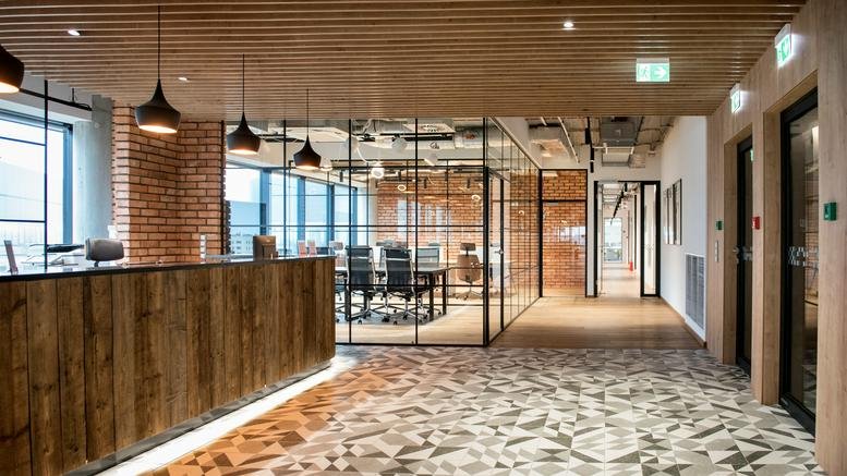 Contemporary wooden reception desk at 18, Aleja Pokoju, Krakow with a view into a glass-walled meeting room.