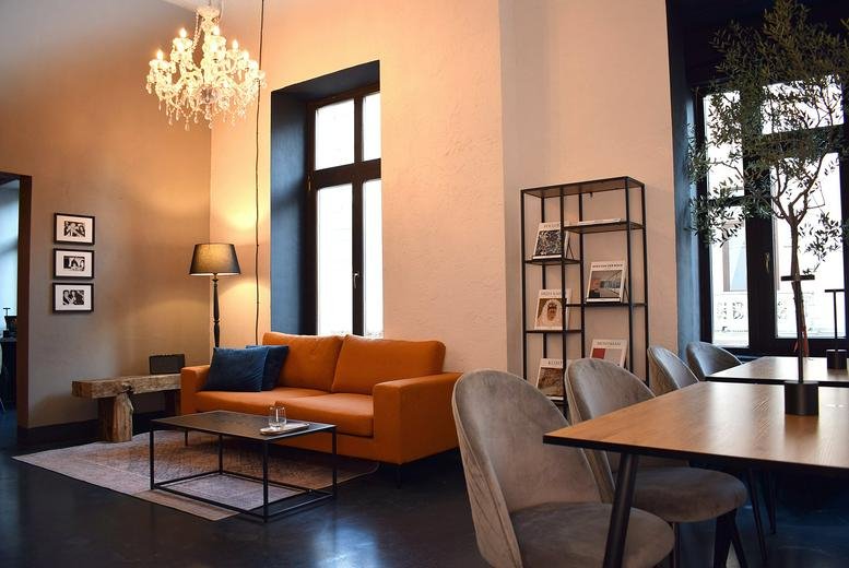 Spacious lounge at Stamina Workspace with an orange sofa, chandelier, and modern shelving.