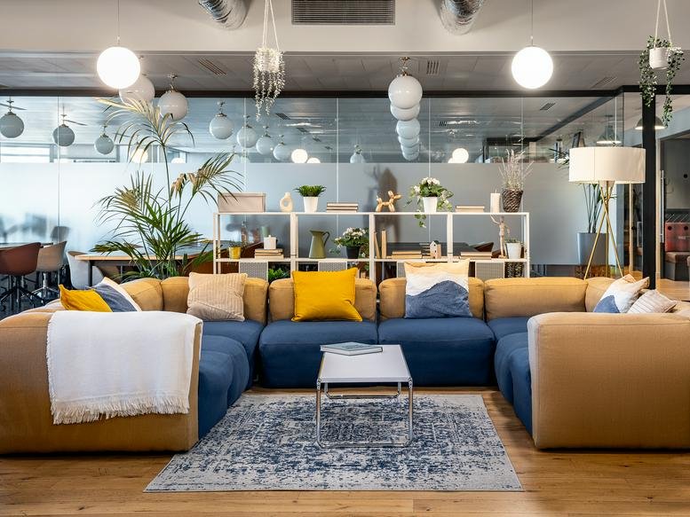 Spacious lounge area with a blue modular sofa, yellow pillows, and decorative plants.