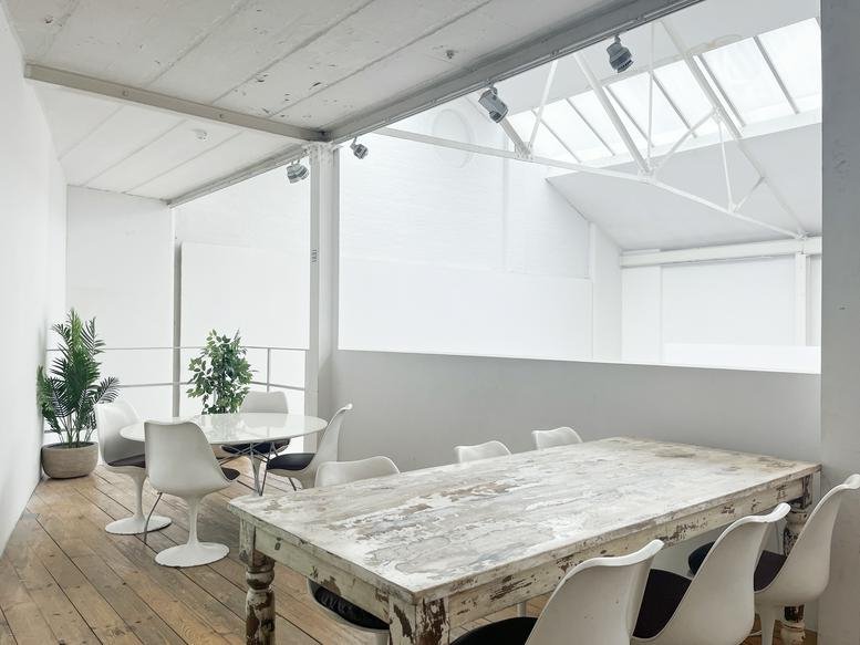 Bright workspace at 3 Loughborough Street with vaulted skylights, wooden floors, and a rustic communal table.
