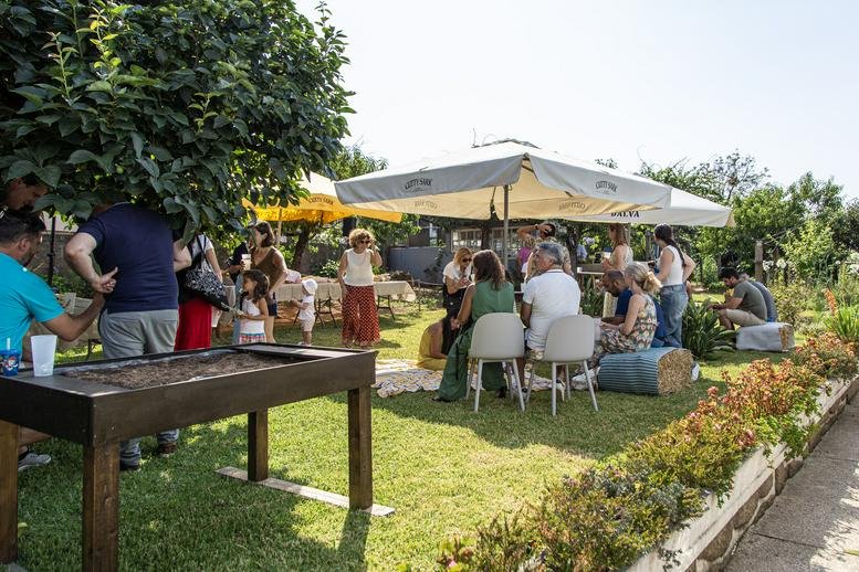 Lively outdoor event with people sitting at tables under large white umbrellas in a garden.