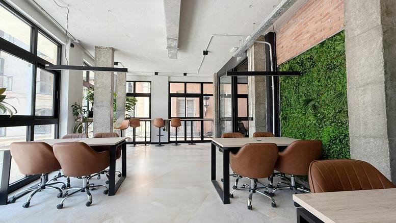 Spacious communal coworking area at 7, Calle Martínez Campos with wooden tables and a lush green plant wall.