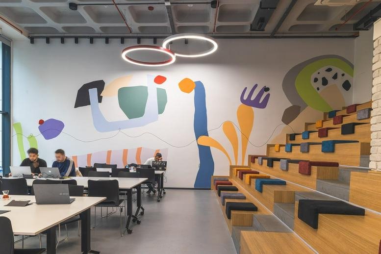 Spacious coworking area at İzQ Girişimcilik Merkezi featuring a vibrant wall mural and tiered wooden seating.