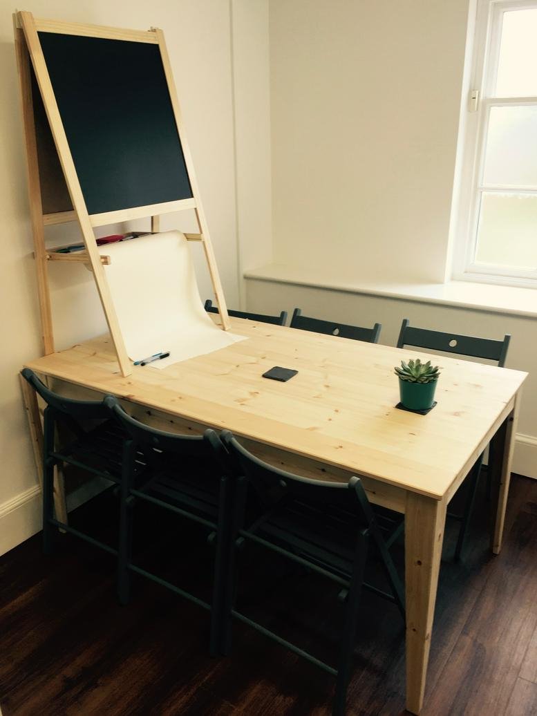 Bright meeting room at Angel Court, 81 St Clement’s featuring a light wood table and a chalkboard easel.