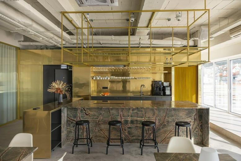 Stylish kitchen and breakout area featuring a marble island, gold shelving, and bar stools.