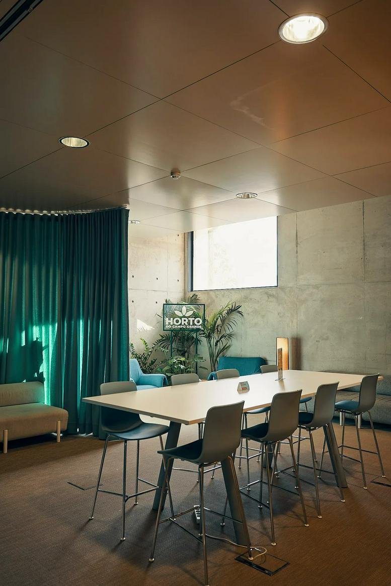 Meeting room at Avenida 24 de Julho 98 with high stools, a large white table, and teal curtains.