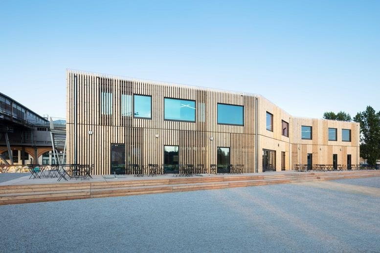 Modern timber-clad exterior of B-PART am Gleisdreieck with a wide paved terrace.