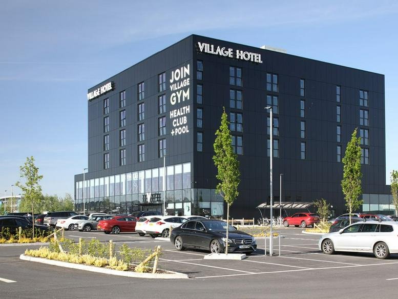Exterior view of the Village Hotel on Bournemouth Road with a modern black facade and parking area.