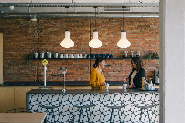 Modern office kitchen with a patterned bar counter, pendant lights, and exposed brick walls.