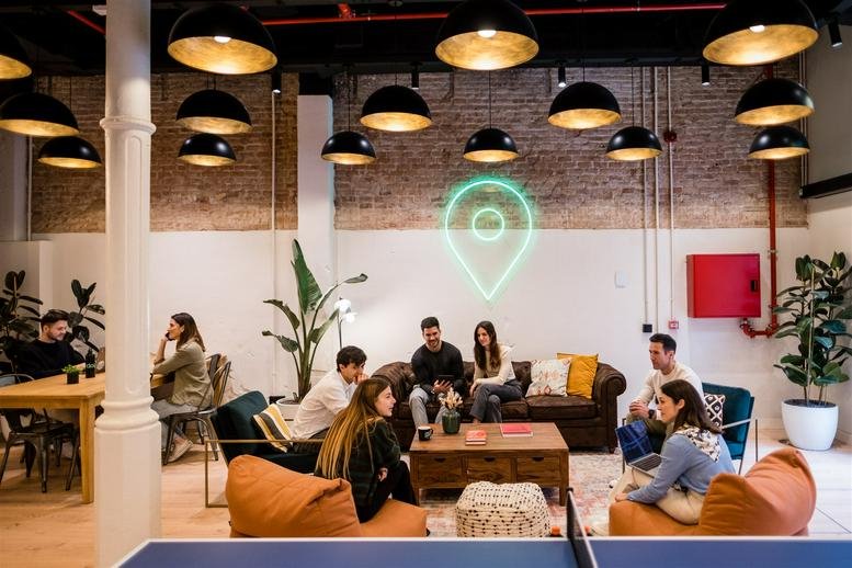 Vibrant coworking lounge with beanbags, green neon sign, and overhead dome lighting.