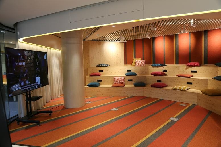 Edifício Atrium Saldanha informal theater-style lounge with wooden tiers, colorful cushions, and striped flooring.