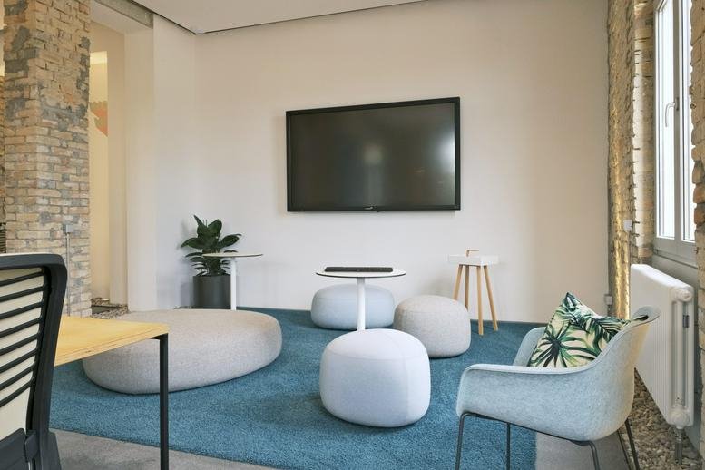 Modern lounge area at Hafenstraße 39 with pebble ottomans, a large wall-mounted screen, and teal rug.