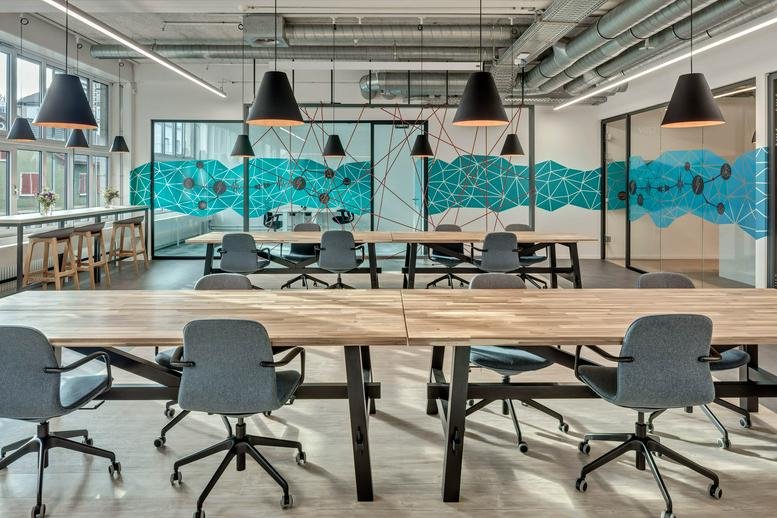 Spacious open-plan workspace at Haselstrasse 16 featuring wooden desks and a blue geometric mural.