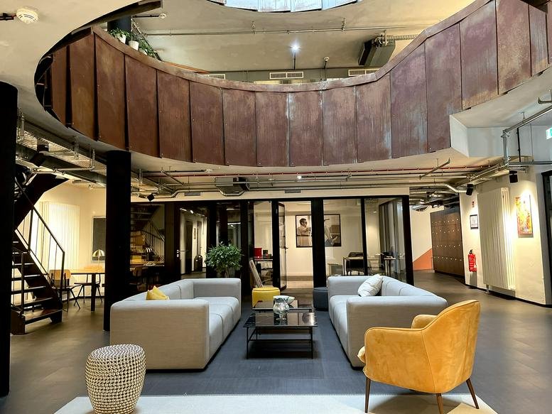 Spacious communal lounge at Hauptstraße 151 featuring gray sofas and a unique curved wood-paneled ceiling element.