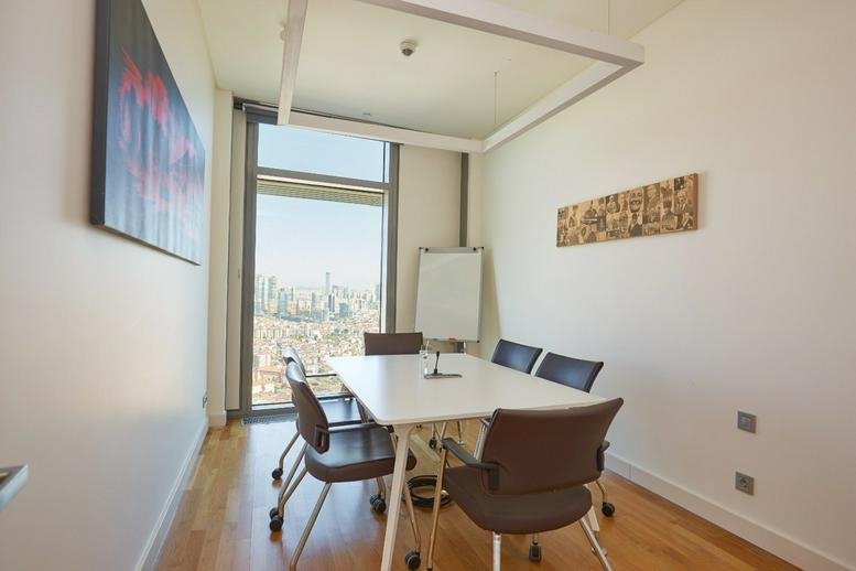 Meeting room at Emaar Square E blok with a white table, modern chairs, and a large window overlooking the city.