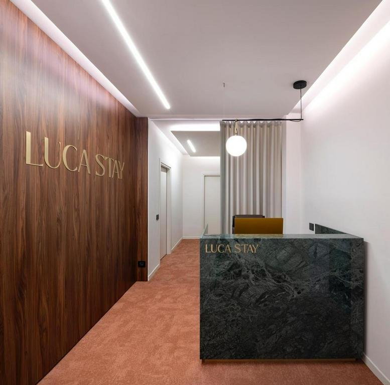 Modern reception lobby at Private Suite, 11 Piazzetta Guastalla, featuring wood paneling and a marble desk.