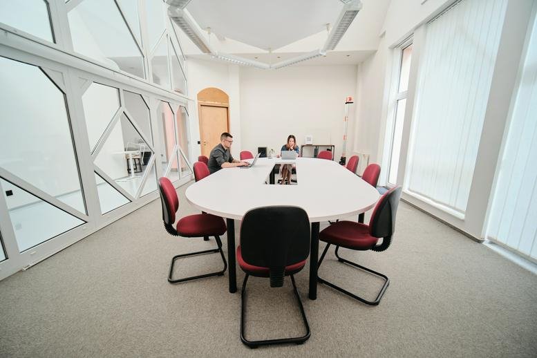 Modern conference room with an oval table and red chairs next to large glass partitions.
