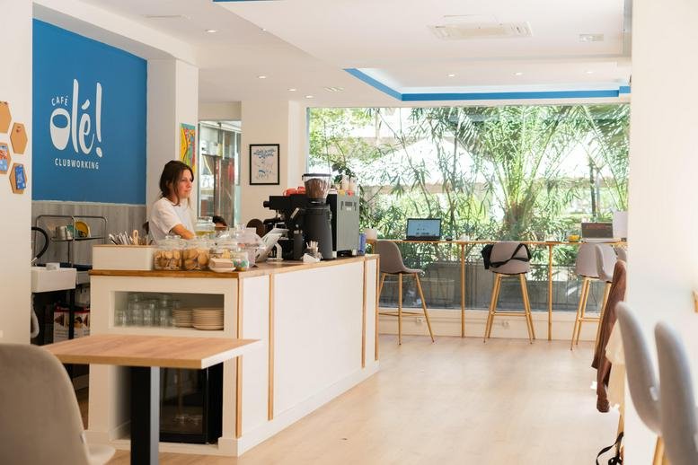 Main lobby and cafe area with high ceilings and views of greenery through large windows.
