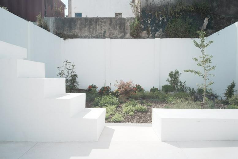 Minimalist white courtyard garden at 185 Rua das Fontainhas with tiered steps and young trees.