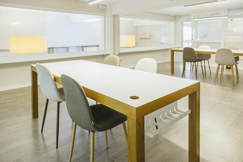 Bright shared workspace at 2, Carrer de Mozart, Barcelona featuring long wooden tables and minimalist chairs.