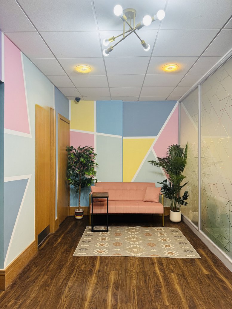 A colorful reception or waiting area featuring a pink sofa, potted plants, and geometric wall art.