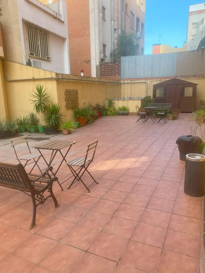 Large tiled outdoor patio area with wooden benches, tables, and various potted plants.