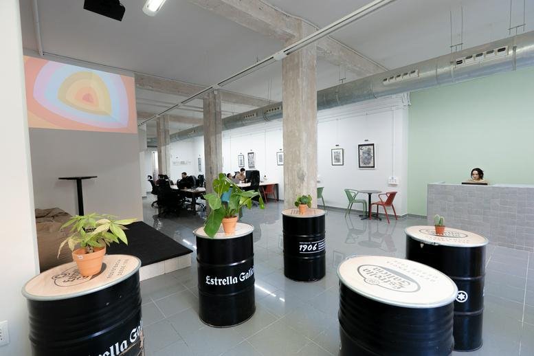 Open-plan workspace featuring barrel tables, a small stage with beanbags, and green accent walls.