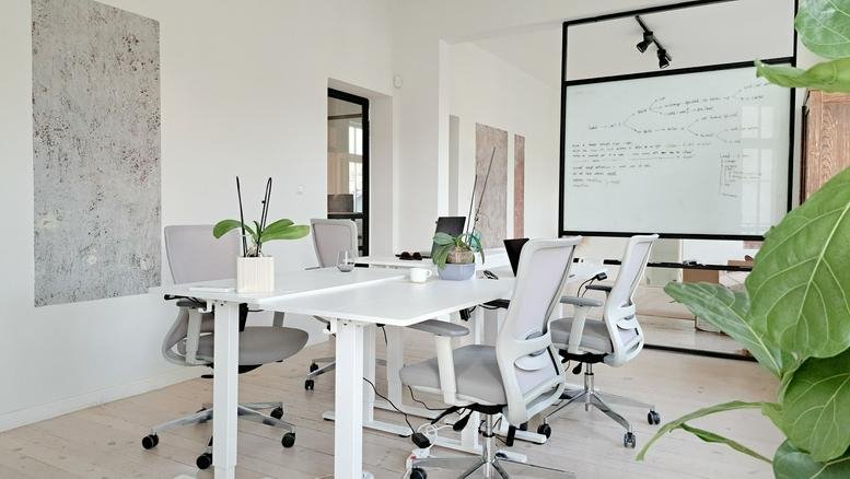 Meeting room with white desks, ergonomic chairs, and a whiteboard.
