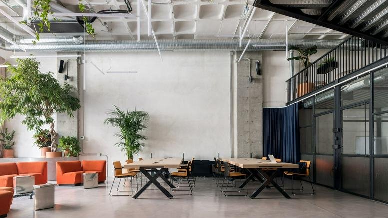 Spacious communal lounge at Area Coworking, 50-52 Calle de Tomás Bretón, with orange sofas and tall indoor trees.