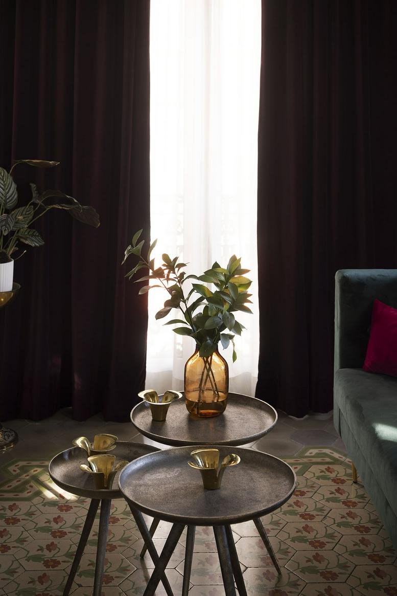 Nesting metal coffee tables with a glass vase and greenery in a sunlit lounge area.