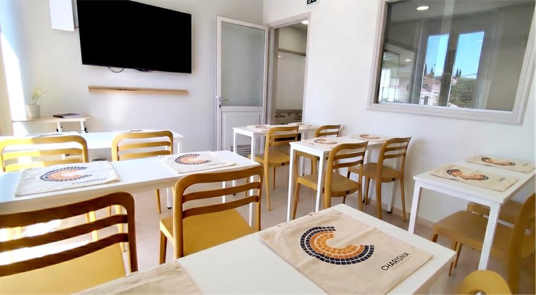 Classroom setup at Charisma International, 1st Floor, Ntaviou, Kanalia, Corfu with white tables and yellow chairs.