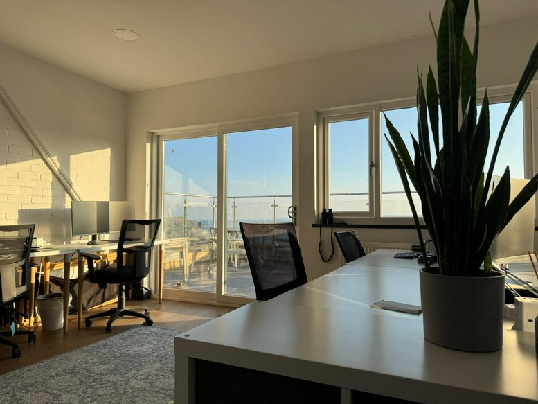 Sunny open-plan office with desks, mesh chairs, and large sliding doors leading to a balcony.