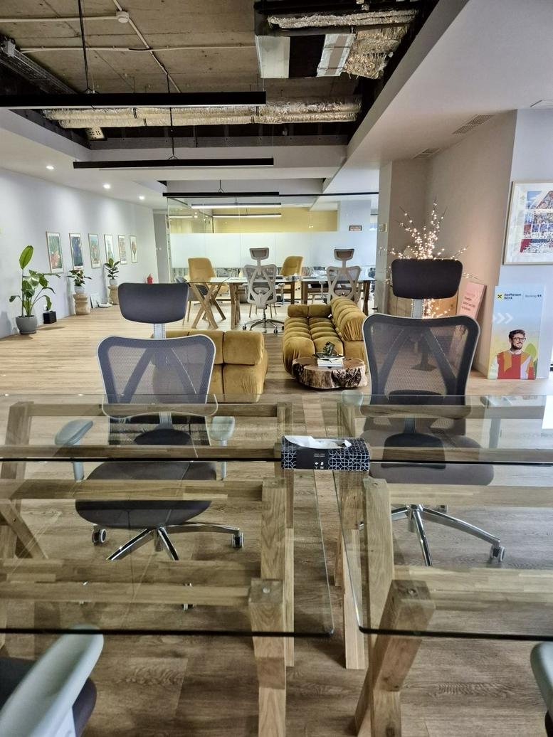 Spacious coworking lounge with glass tables, yellow sofas, and exposed industrial ceiling.